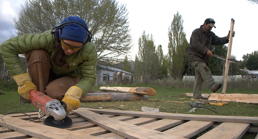 Two people use tools to work on pieces of wood during a service project with outward bound. 